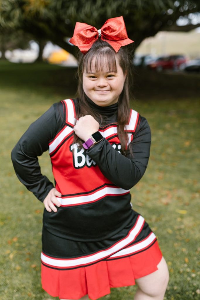 Smiling cheerleader with Down syndrome in vibrant outfit posing confidently outside.