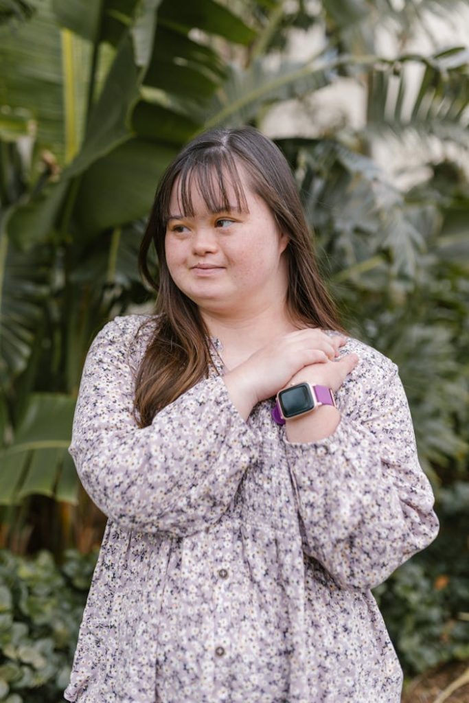 Portrait of a young woman with Down syndrome standing in a lush garden wearing a smartwatch.